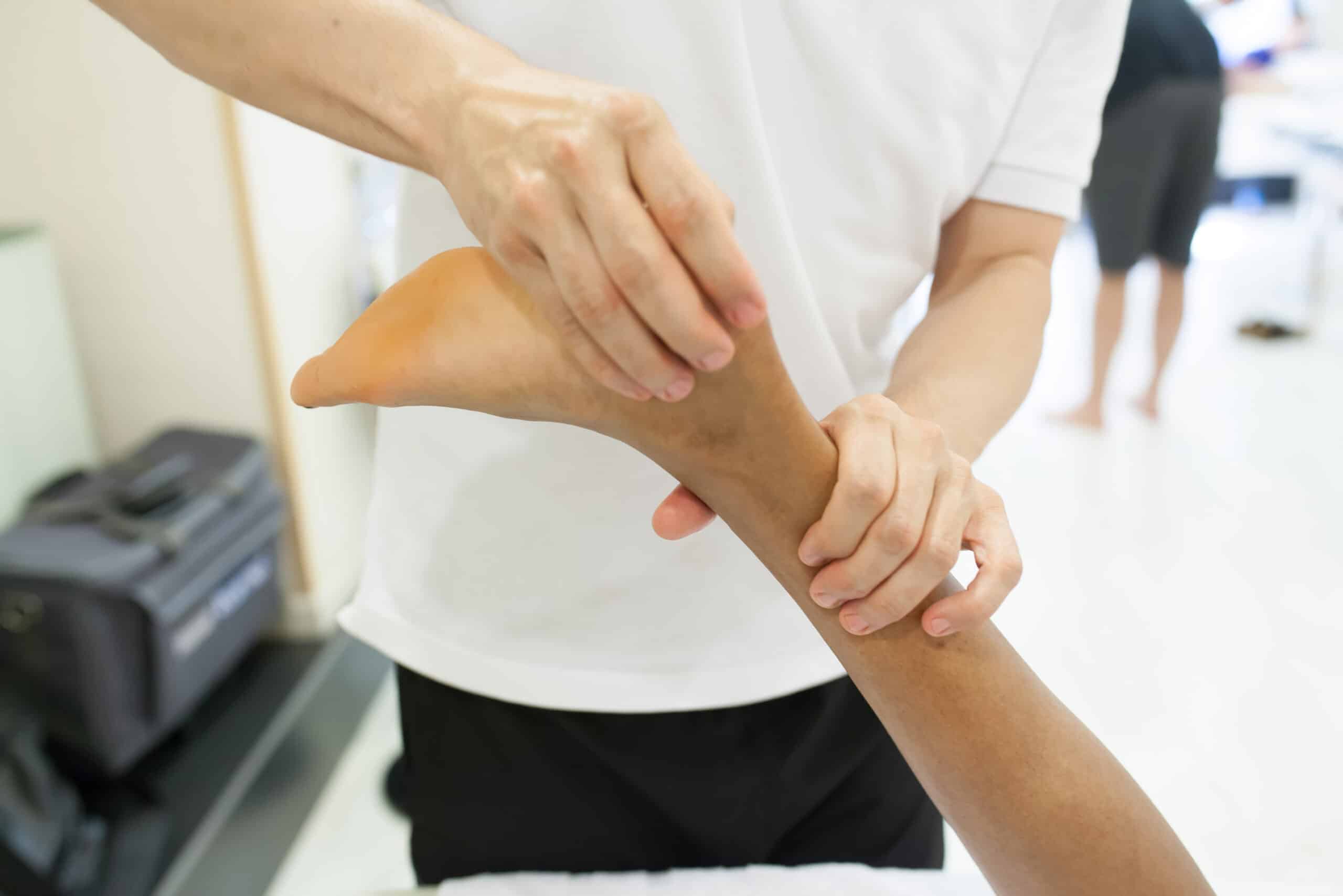 physiotherapist applying massage on Achilles tendon of a man lying on a stretcher upside down