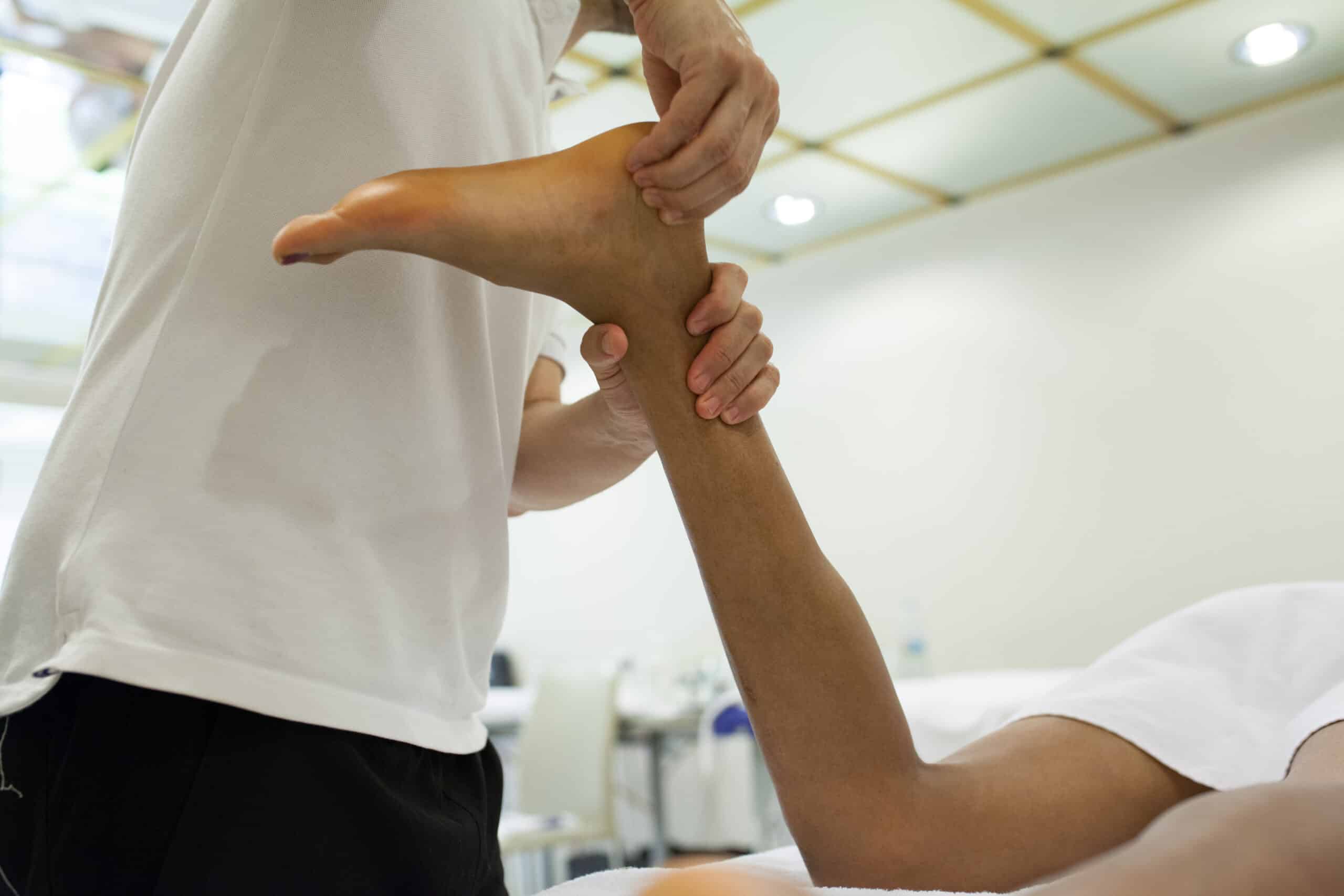 physiotherapist applying massage on Achilles tendon of a man lying on a stretcher upside down